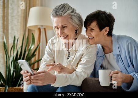 Two older women sitting on a couch, engrossed in a cell phone. Stock Photo