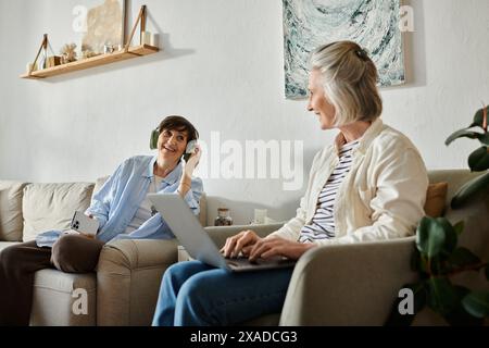 Two women engage in conversation while using a laptop on a cozy couch. Stock Photo