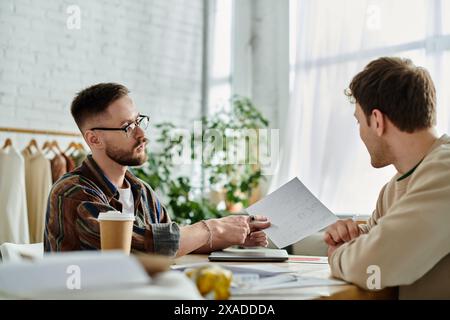 Two men collaborating on designing trendy attire in a workshop. Stock Photo