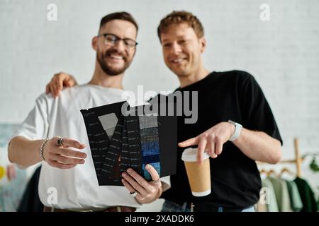 Two men, a gay couple in love, stand side by side in a designer workshop, working together on creating trendy attire. Stock Photo
