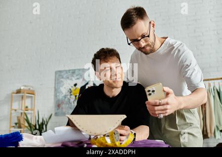 Two men collaborate on a digital device, sharing ideas for trendy attire in a designer workshop. Stock Photo