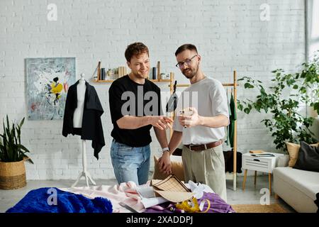Two designers collaborate on a digital device, sharing ideas for trendy attire in a designer workshop. Stock Photo