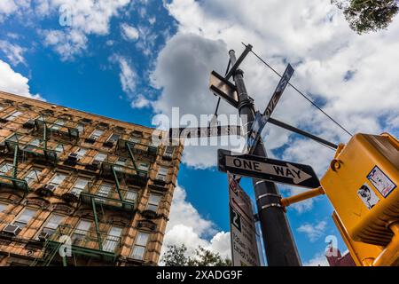 New York City, United States - August 25, 2017: Lamppost with road signs and a traffic light, with a facade with fire stairs in the background (Greenw Stock Photo