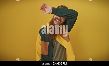 Young redhead man with beard smiling and covering eyes, over yellow background Stock Photo