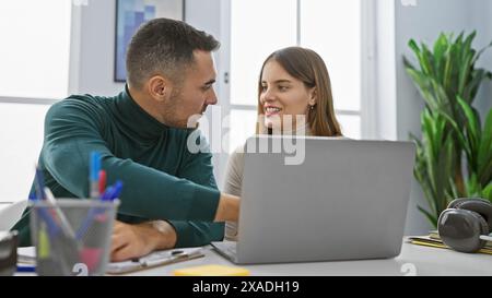 A man and woman engage as colleagues at a modern office, working together on a laptop in an amicable indoor environment. Stock Photo
