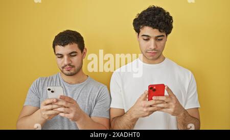 Two men using smartphones against a yellow background, portraying connectivity and casual lifestyle. Stock Photo