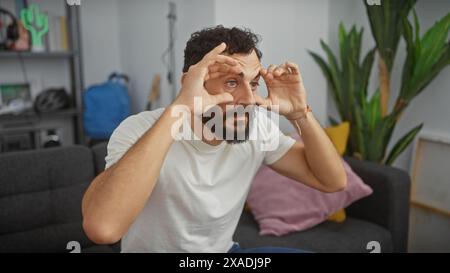 Bearded man sitting indoors rubs tired eyes in a modern apartment living room setting Stock Photo