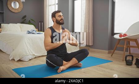 A middle-aged man practices yoga peacefully in a modern bedroom, setting a serene tone. Stock Photo