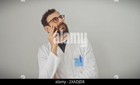 Thoughtful bearded man in lab coat standing against a white wall, embodying professionalism and contemplation. Stock Photo