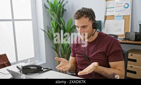 Hispanic man with beard using headset in modern office setting, communicating with clients as customer support representative. Stock Photo