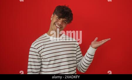 Handsome young hispanic man presents with an extended hand against an isolated red background. Stock Photo