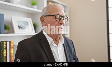 Elegant senior man boss, grey-haired and serious, stands with closed eyes, deep in focused concentration at the office workspace. Stock Photo
