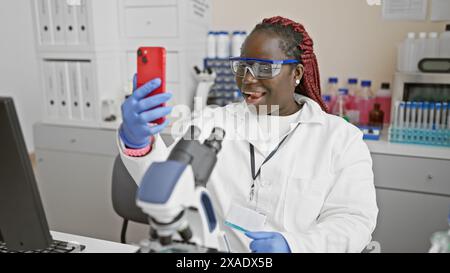 African female scientist conducting a video call on her phone in a laboratory setting. Stock Photo