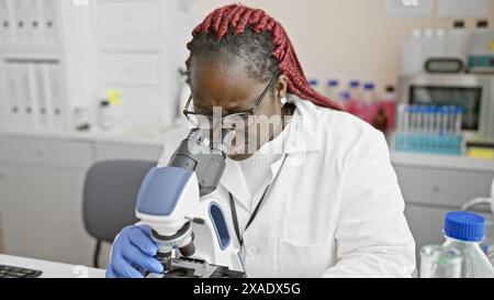 African american woman scientist with braids conducts research using a microscope in an indoor laboratory setting. Stock Photo
