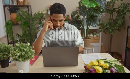 African american man using phone, working with laptop in indoor flower shop. Stock Photo