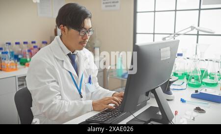 Young asian male scientist working on a computer in a laboratory setting with various equipment in the background. Stock Photo