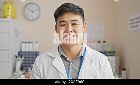 Young asian male scientist in a laboratory setting, smiling at the camera, clad in a lab coat and lanyard. Stock Photo