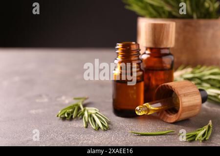 Essential oil in bottles, dropper and rosemary on grey table Stock Photo