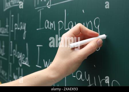 English teacher writing with chalk on green chalkboard, closeup Stock Photo