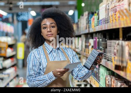 Female store worker in a supermarket aisle holding a digital tablet and checking inventory on the shelves. Stock Photo