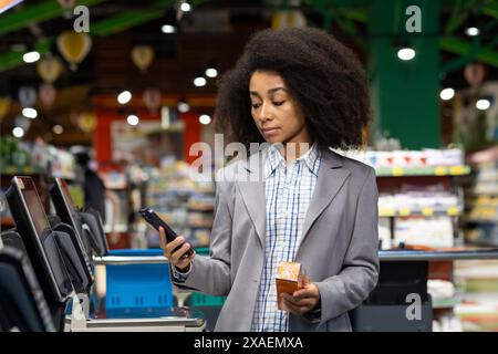 Woman using a mobile phone for scanning items at a self-checkout in a grocery store. Modern technology and convenience shopping. Stock Photo