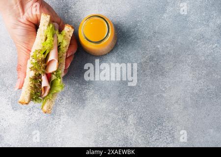 Delicious healthy sandwich for a snack breakfast in women hands. Toast bread tomato ham leaf salad, juice in a bottle Copy space Stock Photo