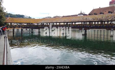 A bridge over a body of water with people walking on it. The bridge is covered in flowers and the water is calm Stock Photo