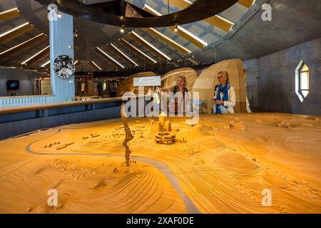A large wooden relief model of the pagan centre of Old Uppsala lies beneath a curved exhibition roof at the Gamla Uppsala Museum, journalist Angela Berg (right) and another visitor examining and discussing it. More than 2,000 people were buried in small and large mounds. Disavägen, Uppsala, Uppsala County, Sweden. Stock Photo