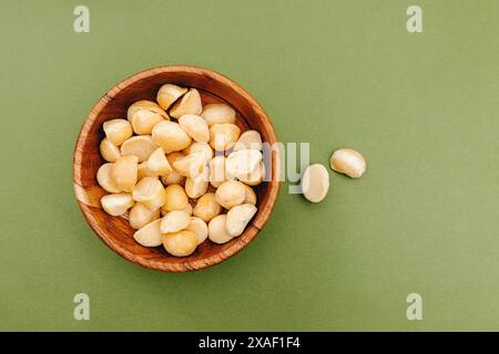 Macadamia nuts in a small wooden bowl on green background, top view Stock Photo