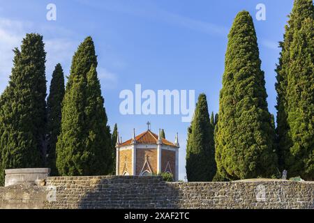 photo of an small red brick and white gothic chapel surrounded by cypress under blue sky on sunny day Stock Photo
