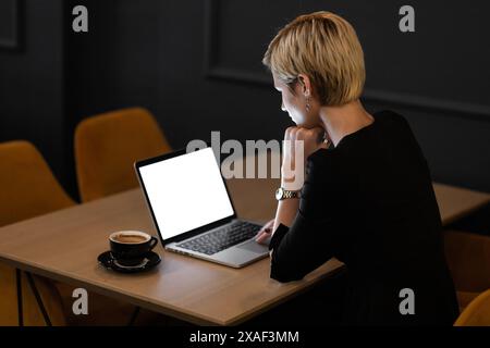A focused professional woman works on her laptop in a stylishly decorated office space, showcasing a modern aesthetic with a coffee cup beside her. Stock Photo