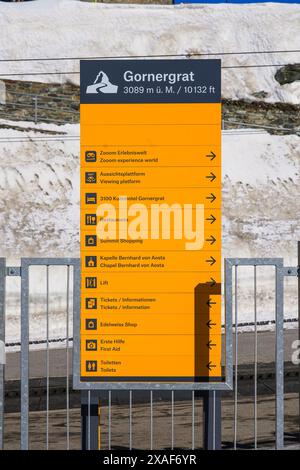 Yellow directional sign pointing at the tourist facilities of the Gornergrat summit facing the Matterhorn in the Pennine Alps, Canton of Valais, Switz Stock Photo