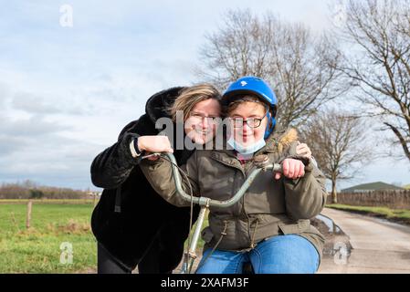 Happy girl with Down Syndrome driving the tricycle with her friend in the Flanders fields, Hakendover, Flanders, Belgium. Model released Stock Photo