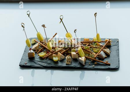 Slicing different types of cheese and grapes. Appetizer with cheese and grapes on a black board on a white background Stock Photo