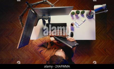 Top down view of software programmer finishing remote job shift, packing backpack, leaving office after finishing project. Aerial shot of IT admin putting laptop in bag, sitting up from desk chair Stock Photo