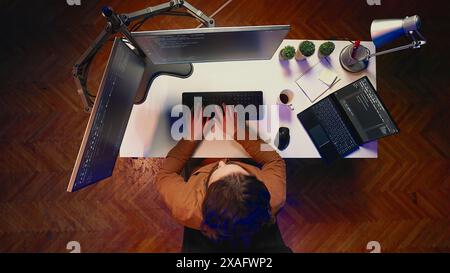 Top down view of remote worker typing code in personal office, using javascript language to develop software application. It specialist using multimonitor desktop setup to finish project, aerial shot Stock Photo