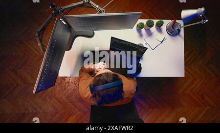 Top down view of developer typing complex code in home office, listening music and developing software application. IT expert wearing headphones, solving coding project tasks on laptop, aerial shot Stock Photo