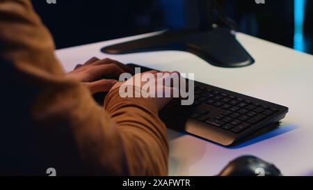 Computer scientist listening music while writing lines of code during remote job shift in home office. IT specialist enjoying audio podcast, coding on desktop PC, camera A extreme close up Stock Photo