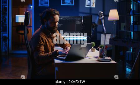 Computer scientist putting headphones on while developing code on PC, making time pass faster during remote job shift. IT admin doing multitasking in home office while listening music, camera B Stock Photo