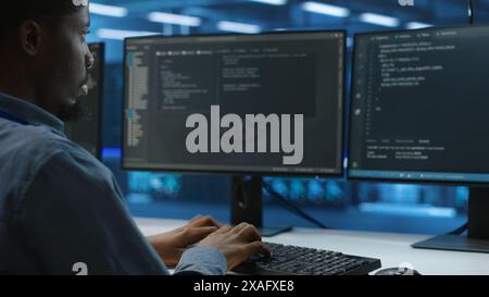 Technician doing system analysis, typing data on PC, doing needed adjustments in supercomputers server farm housing advanced data storage infrastructure supporting critical IT workloads, close up Stock Photo