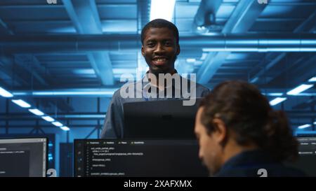 Portrait of cheerful african american manager supervising team in server room providing computing resources for workloads. Jolly supervisor oversees technicians in data center mending supercomputers Stock Photo