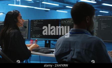 Woman talking in headphone mic, doing system analysis of server farm supercomputers. IT support worker in remote call using headset microphone in data center housing storage infrastructure Stock Photo