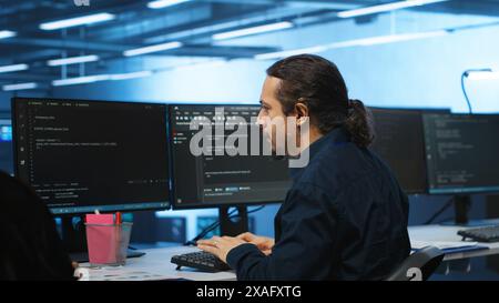 Knowledgeable engineer upgrading equipment in data center, zoom in shot. Specialist at PC desk in high tech establishment overseeing server rows, typing on keyboard, close up shot Stock Photo