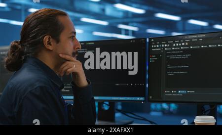 Computer scientist in server hub doing system analysis, coding, doing needed adjustments for supercomputers to run. Expert working in data center housing advanced storage infrastructure Stock Photo