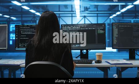 IT support employee in data center putting headphones on to talk with coworkers, coding on computer. Woman in remote call meeting with colleagues using headset microphone, overseeing server clusters Stock Photo