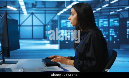 IT engineer looking at PC screen, working in network security data center, ensuring optimal performance. Woman monitoring energy consumption across operational server rigs components, close up shot Stock Photo
