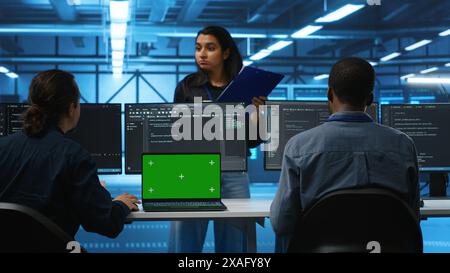Isolated screen laptop in front of IT support workers coding on computers and talking with managers, upgrading equipment. Engineers at PC desk overseeing server clusters using chroma key notebook Stock Photo