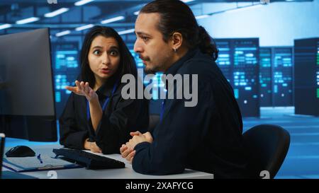 IT technicians in server farm brainstorming ways to repair equipment storing datasets. Colleagues at work in data center discussing how to mend rigs doing computational operations Stock Photo