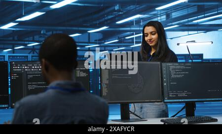Cheerful supervisor in server room managing multiethnic team of technicians looking for equipment misconfigurations. Upbeat team leader coordinating workers fixing data center malfunctions Stock Photo