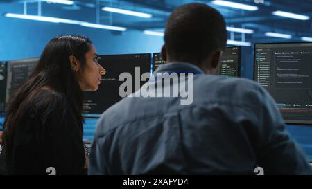 Diverse IT engineers in server room brainstorming ways to fix equipment storing datasets. Multiethnic coworkers discussing how to mend data center racks doing complex computational operations Stock Photo
